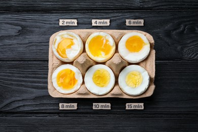 Image of Boiled chicken eggs of different readiness stages in carton on black wooden table, top view