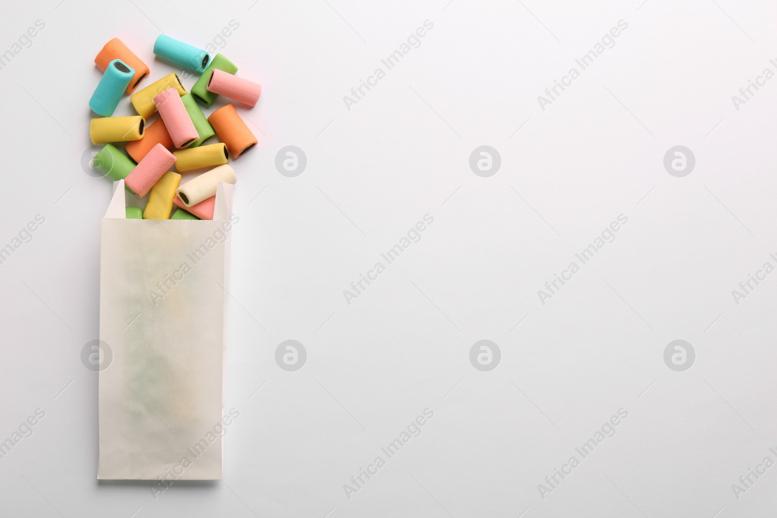 Photo of Paper bag with tasty liquorice candies on light background, top view. Space for text