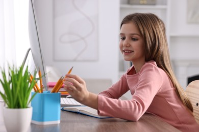 Photo of E-learning. Cute girl using computer during online lesson at table indoors