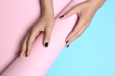 Photo of Woman with black manicure holding paper roll on color background, closeup. Nail polish trends