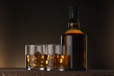 Whiskey with ice cubes in glasses and bottle on wooden table