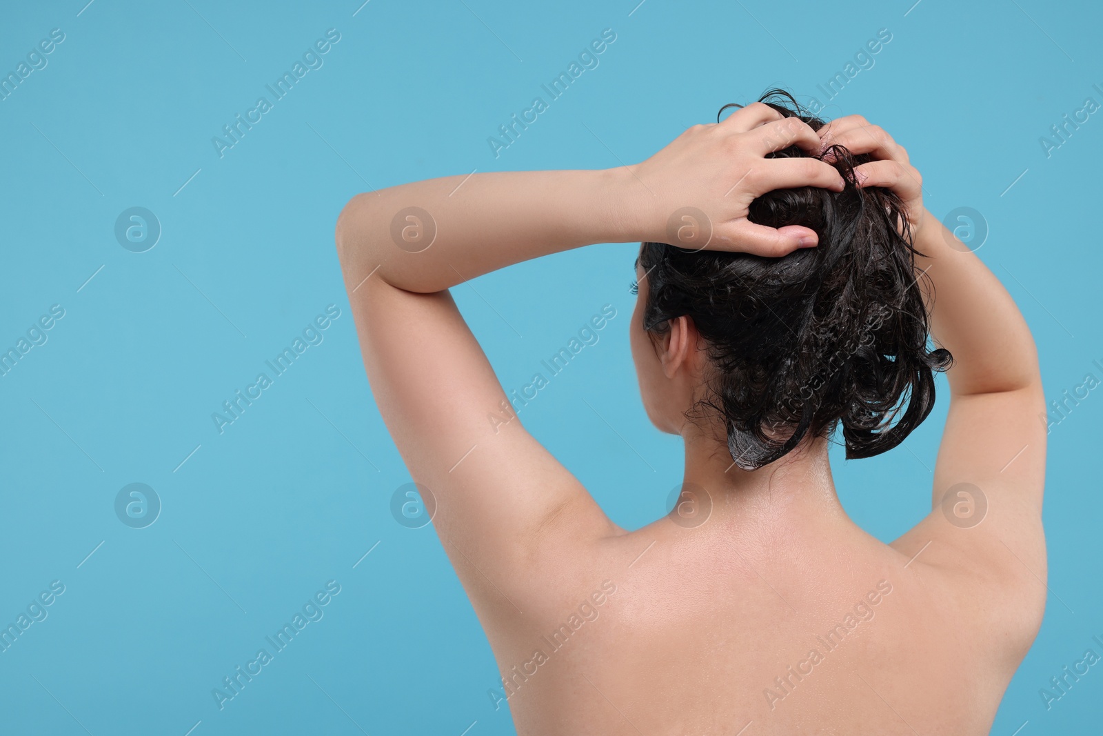 Photo of Woman washing hair on light blue background, back view. Space for text