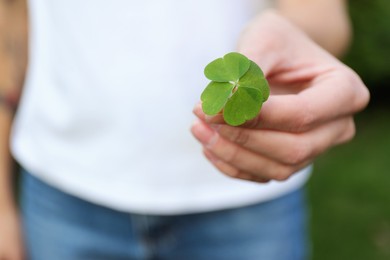 Photo of Woman holding beautiful green four leaf clover outdoors, closeup. Space for text