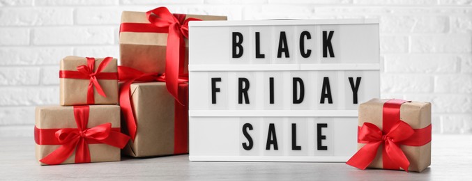 Image of Lightbox with words Black Friday Sale and gift boxes on wooden table against white brick wall. Banner design