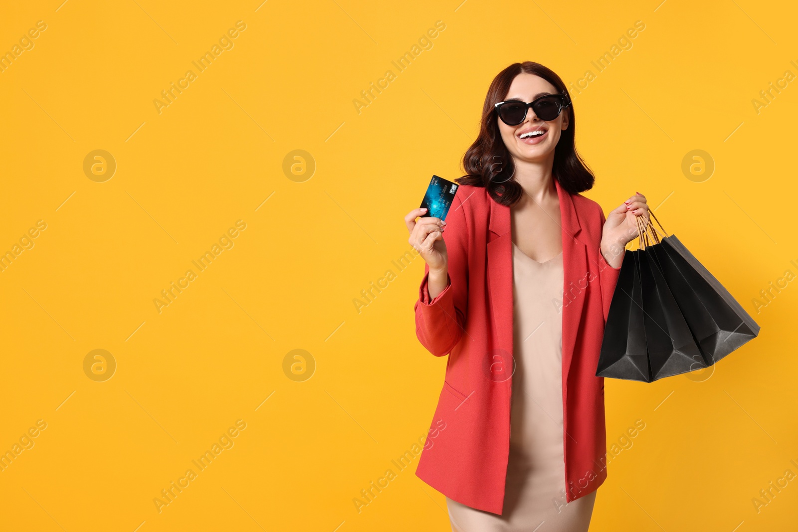 Photo of Beautiful young woman with paper shopping bags and credit card on yellow background. Space for text