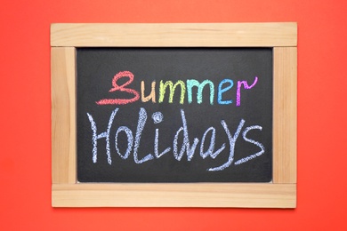 Photo of Chalkboard with phrase SUMMER HOLIDAYS on coral background, top view. School's out