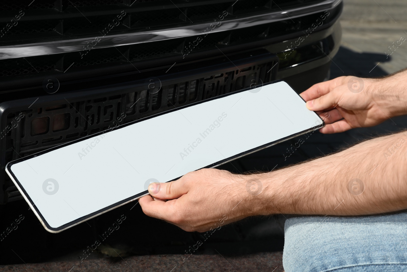 Photo of Man installing vehicle registration plate outdoors, closeup