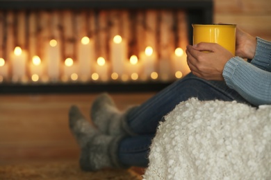 Woman with cup of hot drink near decorative fireplace indoors, closeup. Winter atmosphere