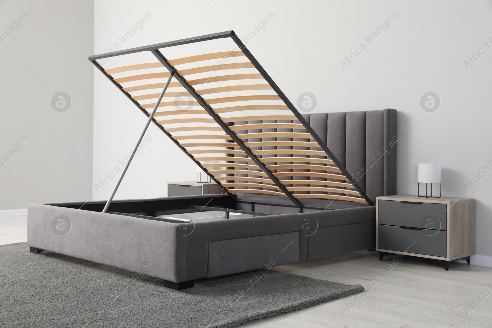 Photo of Comfortable bed with storage space for bedding under lifted slatted base in room