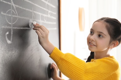 Photo of Little girl writing music notes on blackboard in classroom, closeup