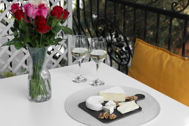 Beautiful roses, glasses of wine and snacks on white table at balcony