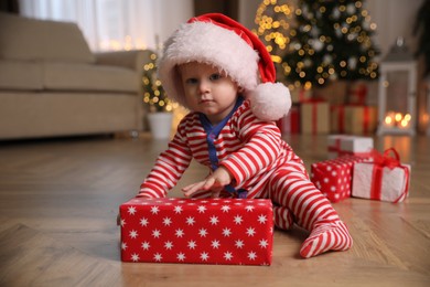 Photo of Baby in Christmas pajamas and Santa hat near gift box  indoors