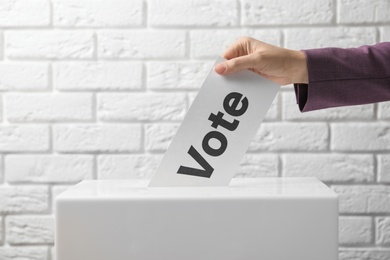 Photo of Woman putting her vote into ballot box against brick wall, closeup