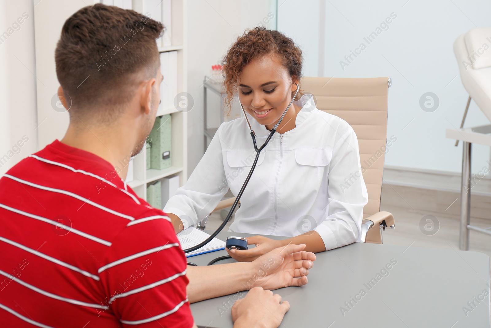 Photo of Doctor checking patient's blood pressure at table in office