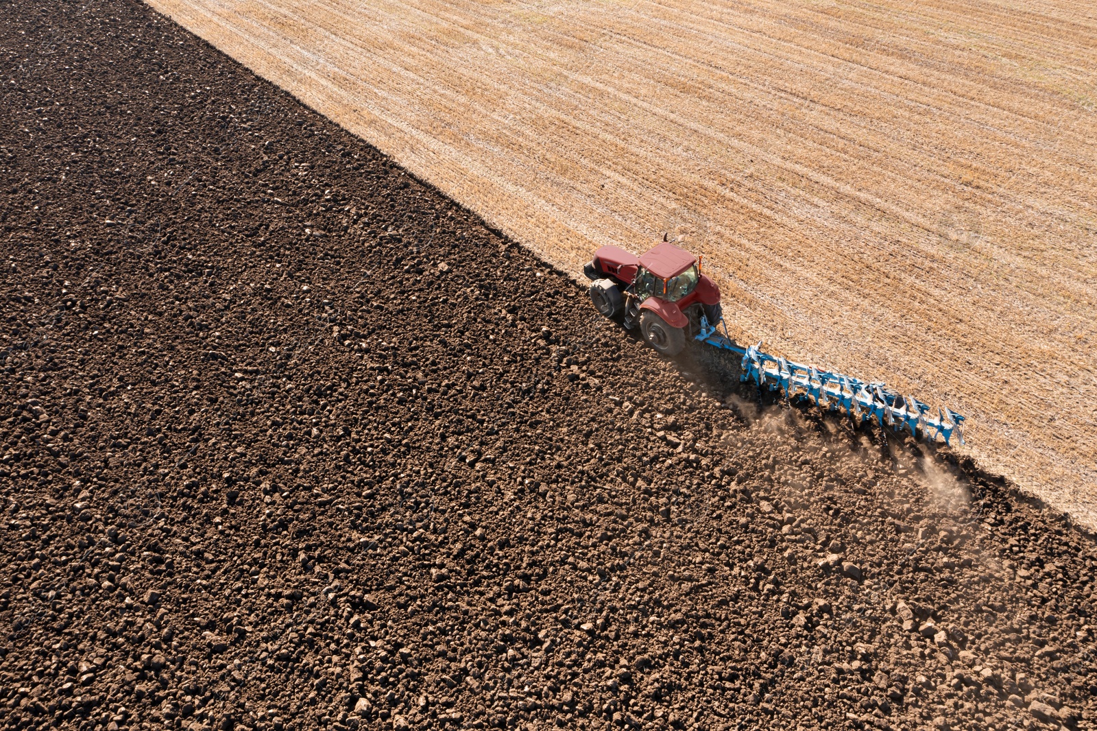 Image of Tractor pulling plow in agricultural field on sunny day, aerial view