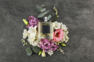 Bottle of luxury perfume and floral decor on dark grey table, top view