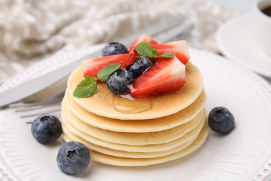 Photo of Delicious pancakes with strawberries, blueberries and mint on plate, closeup