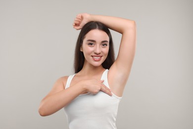 Beautiful young woman doing breast self-examination on light grey background