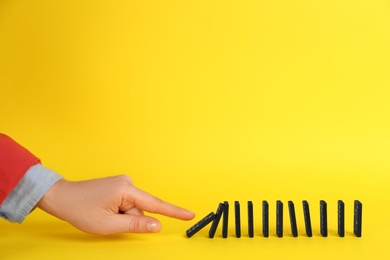 Photo of Woman causing chain reaction by pushing domino tile on yellow background, closeup. Space for text