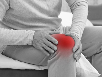 Man suffering from pain in knee at home, closeup. Black and white effect