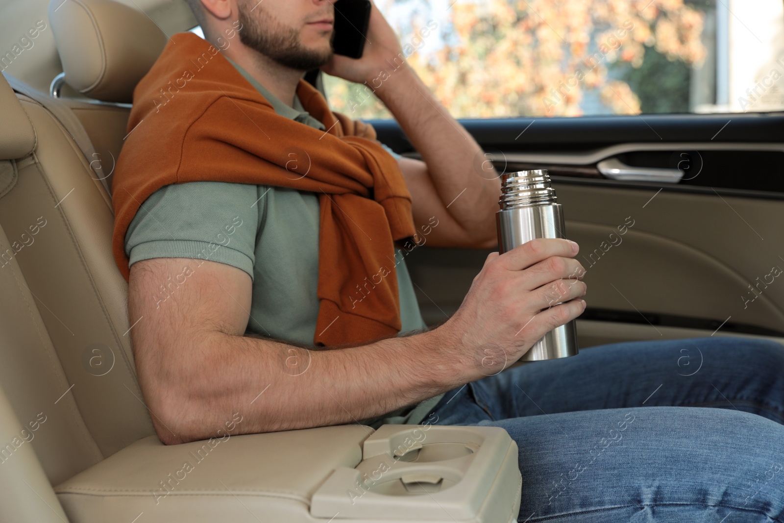Photo of Man with thermos talking on phone in car, closeup