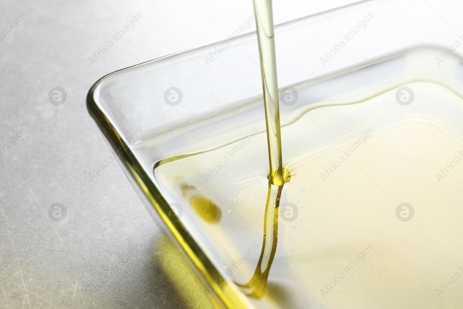 Photo of Pouring fresh olive oil into bowl on grey background, closeup