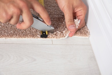 Photo of Man cutting new carpet flooring indoors, closeup. Space for text