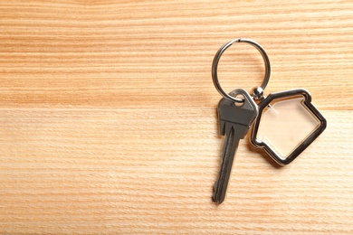 Key with trinket in shape of house on wooden background. Real estate agent services