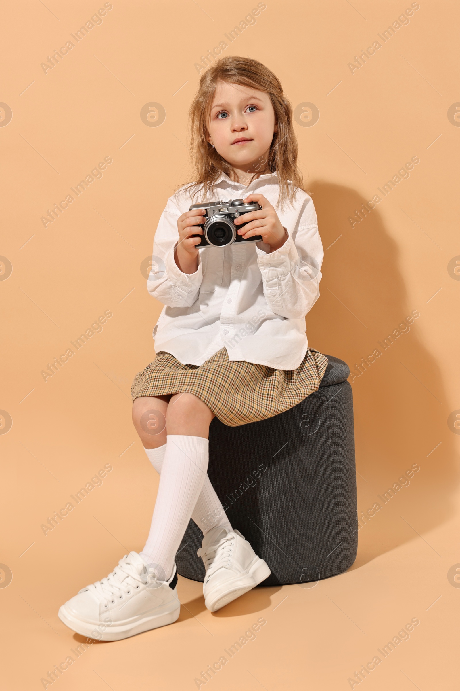 Photo of Fashion concept. Stylish girl with vintage camera on pale orange background