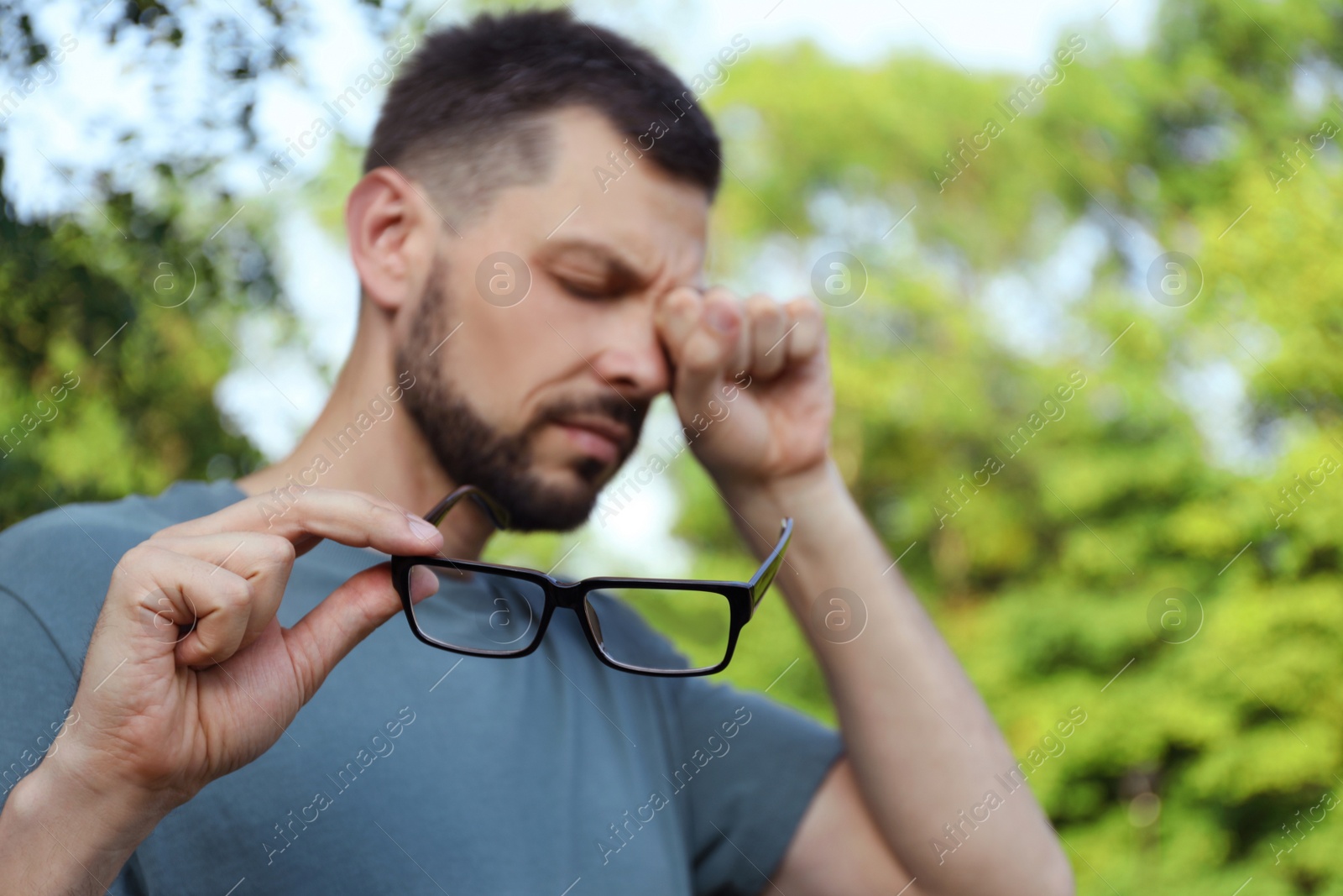 Photo of Man suffering from eyestrain outdoors, focus on hand with glasses