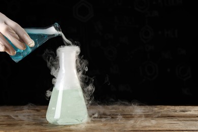 Scientist working with laboratory glassware and space for text at wooden table, closeup. Chemical reaction