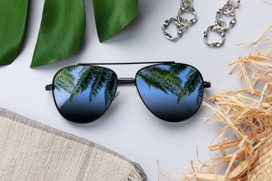 Image of Flat lay composition with sunglasses on white background. Sky and palm trees reflecting in lenses