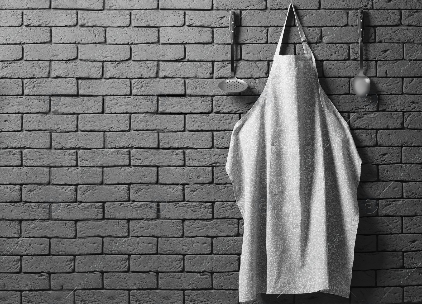 Photo of Clean apron with pattern and kitchen tools on grey brick wall