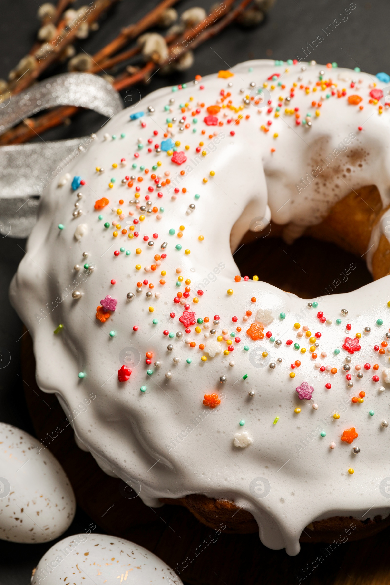 Photo of Delicious Easter cake decorated with sprinkles near eggs on table, closeup