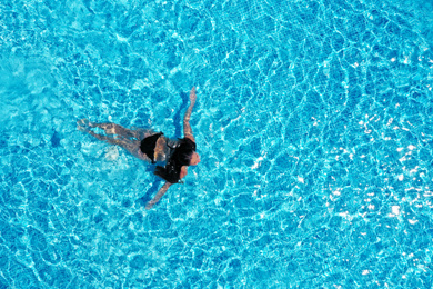 Image of Beautiful young woman swimming in pool, top view. Space for text