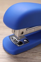 One blue stapler on wooden table, closeup