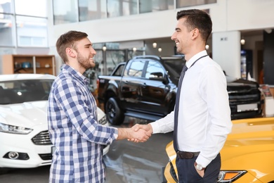 Photo of Young man shaking hands with salesman in car salon