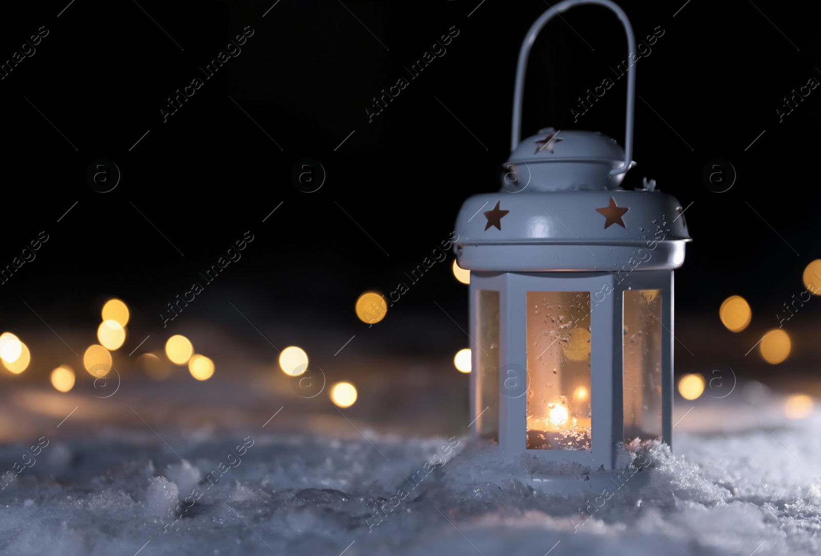 Photo of Lantern with burning candle and Christmas lights on white snow outdoors. Space for text