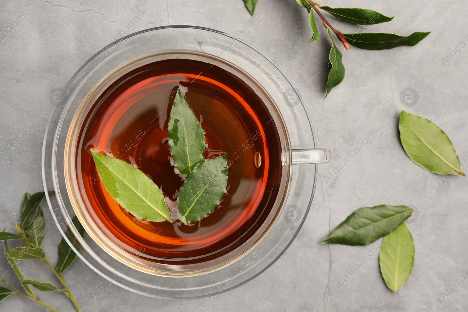 Photo of Cup of freshly brewed tea with bay leaves on grey table, flat lay