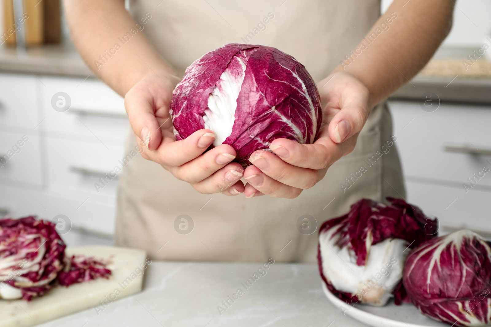 Photo of Woman holding fresh ripe radicchio indoors, closeup