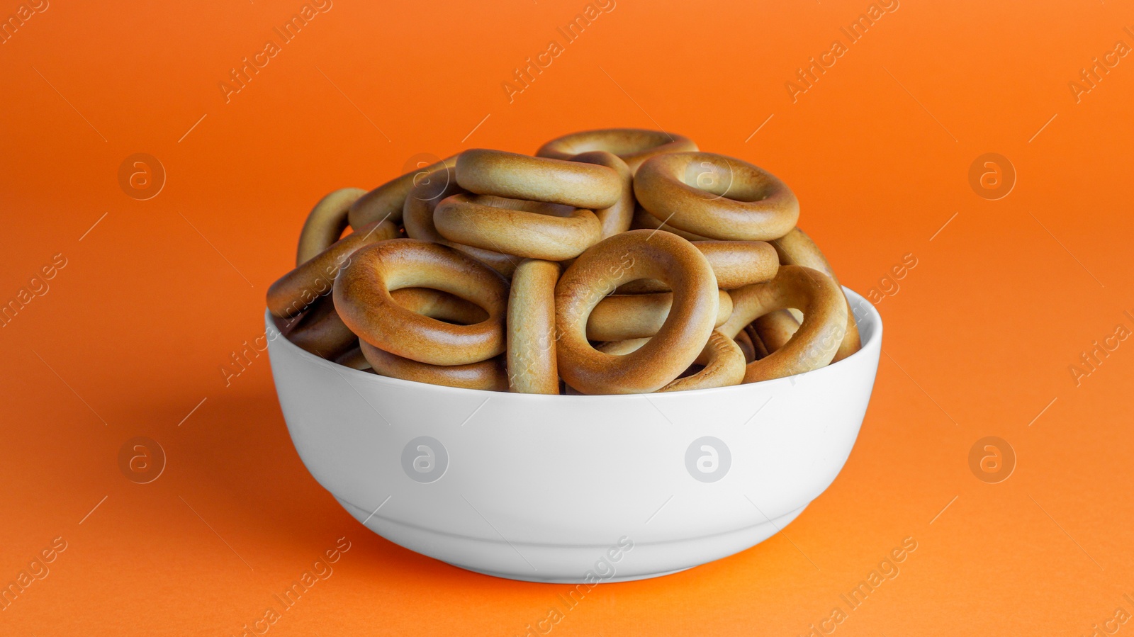 Photo of Bowl of tasty dry bagels (sushki) on orange background