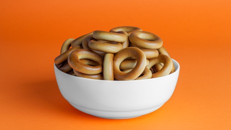 Photo of Bowl of tasty dry bagels (sushki) on orange background