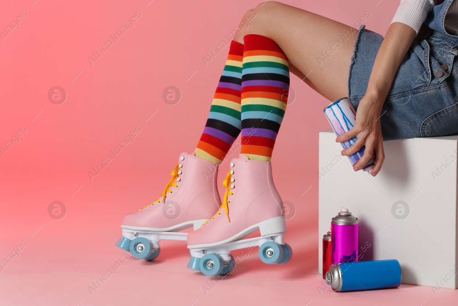 Photo of Woman with vintage roller skates and spray paint cans on color background, closeup. Space for text
