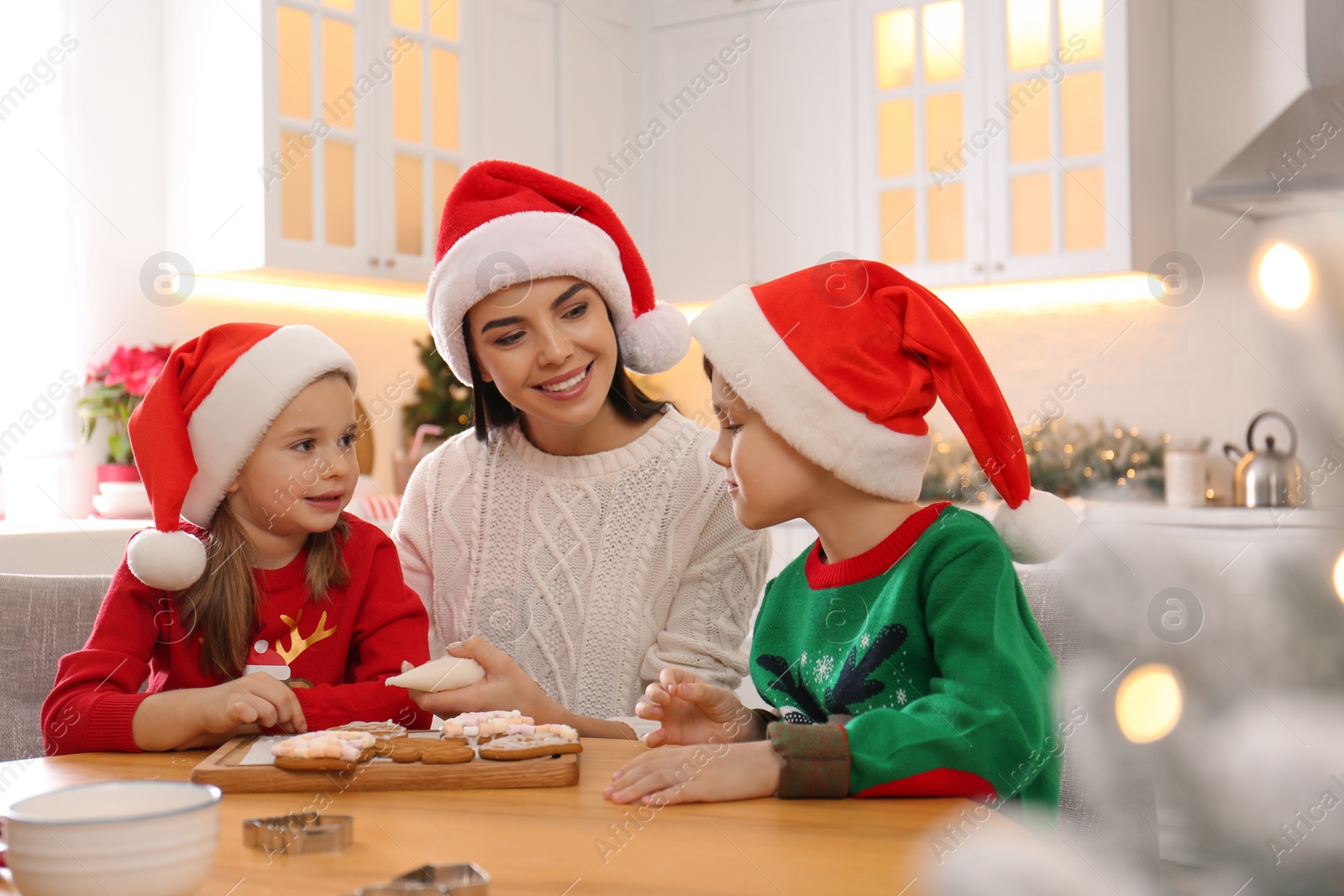 Photo of Mother and her cute little children decorating tasty Christmas cookies at table in kitchen