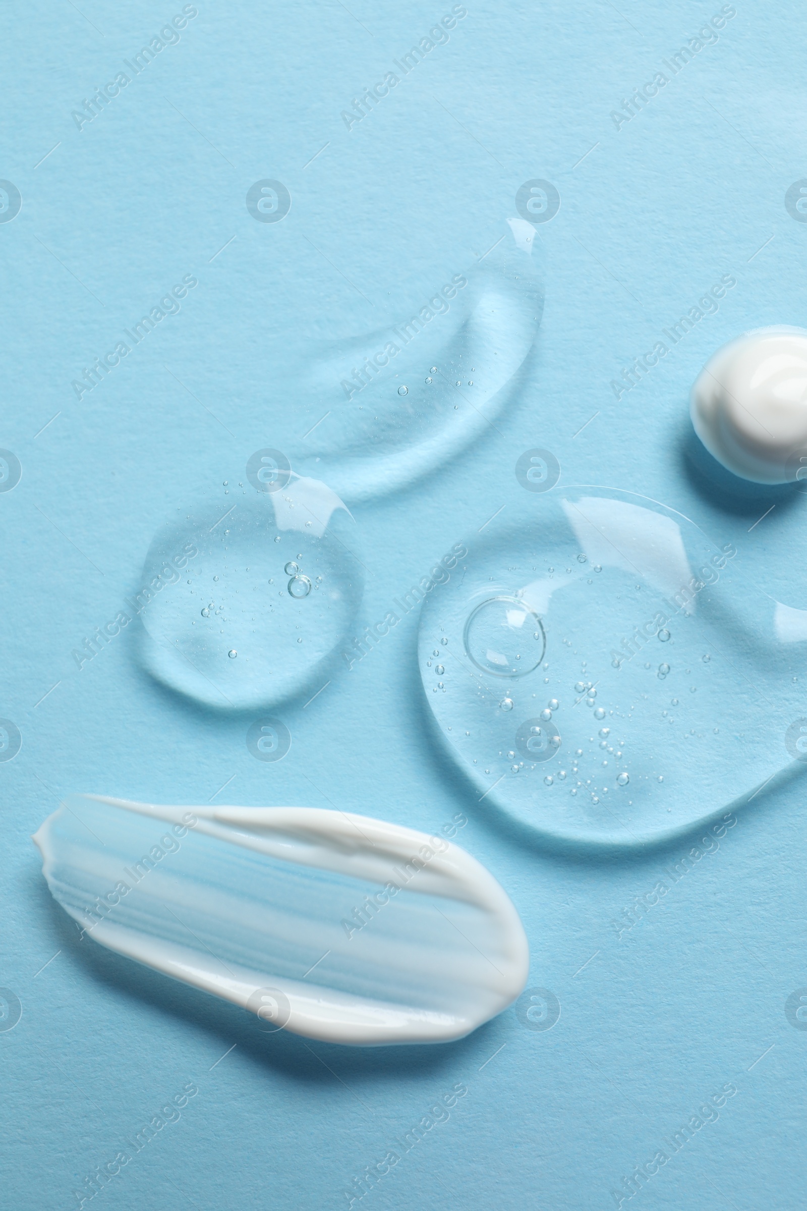 Photo of Samples of transparent gel and white cream on light blue background, flat lay