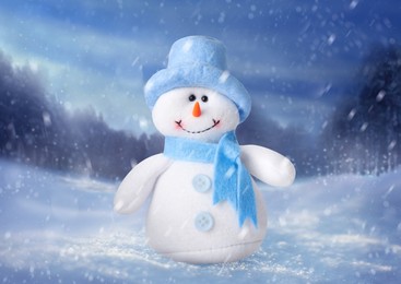 Image of Cute decorative snowman in blue hat and scarf outdoors on snowy day