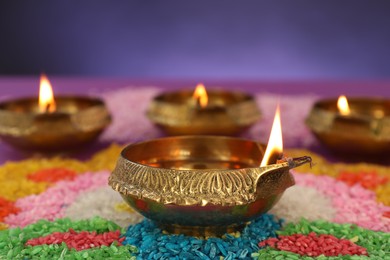 Diwali celebration. Diya lamps and colorful rangoli on blurred background, closeup