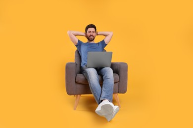 Photo of Happy man with laptop sitting in armchair against yellow background