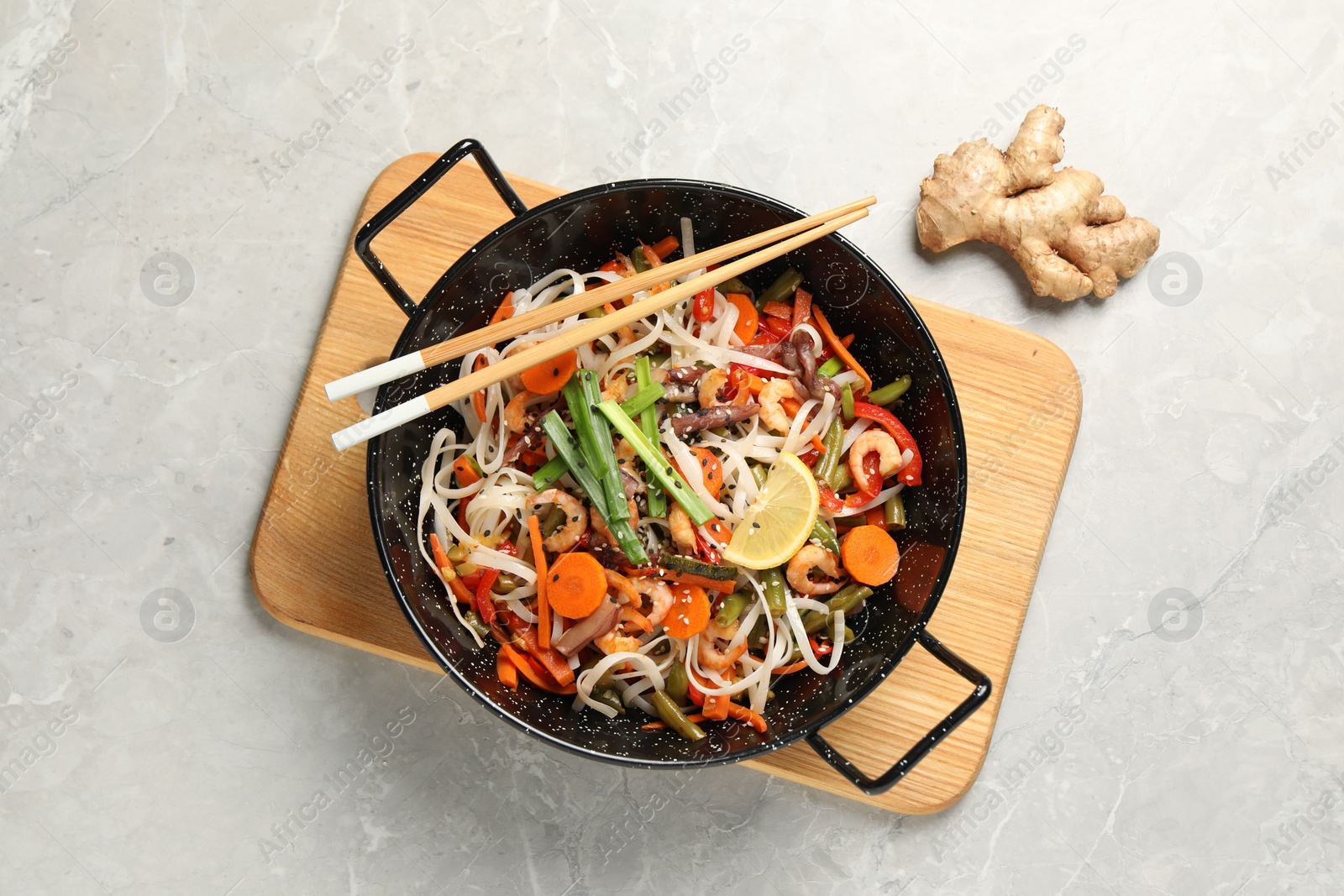 Photo of Shrimp stir fry with noodles and vegetables in wok on grey table, top view