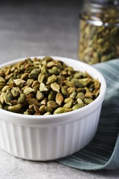 Ceramic bowl with dry cardamom on grey table, closeup